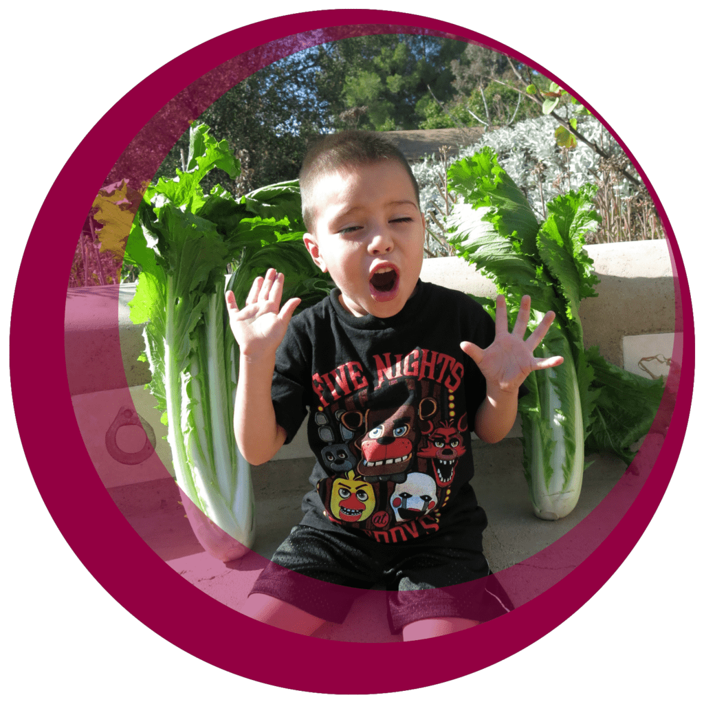 an excited boy sits next to some large bunches of lettuce